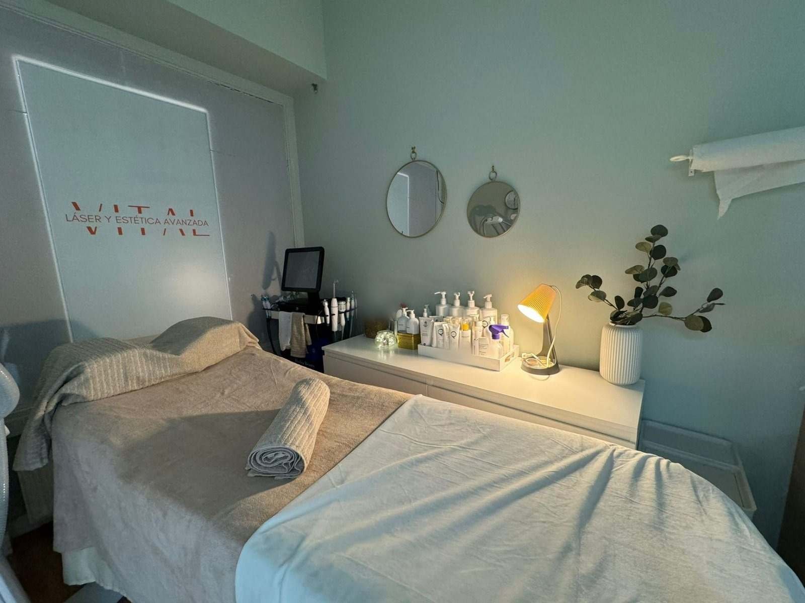 Camilla preparada en una cabina de Vital, con espejos redondos y plantas en la pared